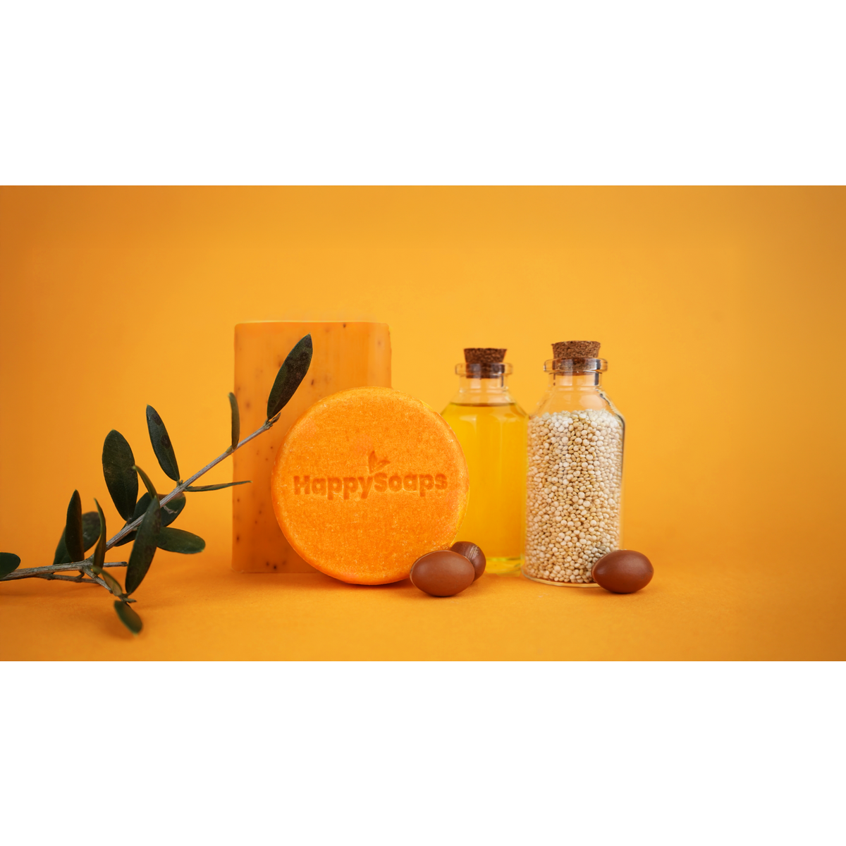 Oranje HappySoaps shampoo bar met decoratieve flesjes en een tak op een oranje achtergrond